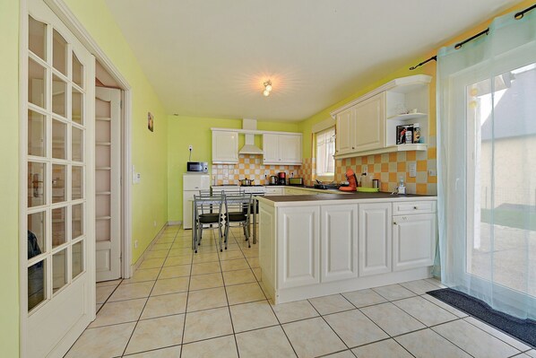 A kitchen with white cabinets, a dining area with chairs, and a window with a curtain.