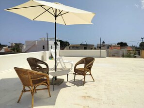 Une terrasse sur le toit, avec des fauteuils en osier, une table et un grand parasol.
