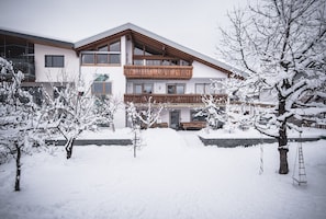 A two-story building with a wooden balcony, snow-covered trees, and a stone wall.