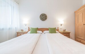 A double bed with green pillows, two bedside tables with lamps, a wooden wardrobe, and a wall-mounted decorative item.