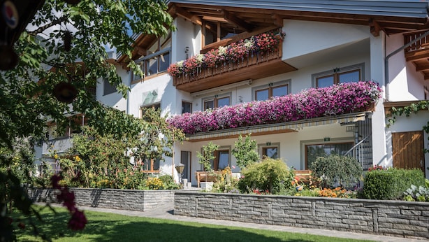 Un edificio a più piani con balconi decorati da fiori, un muro di sostegno in pietra e un prato ben curato.