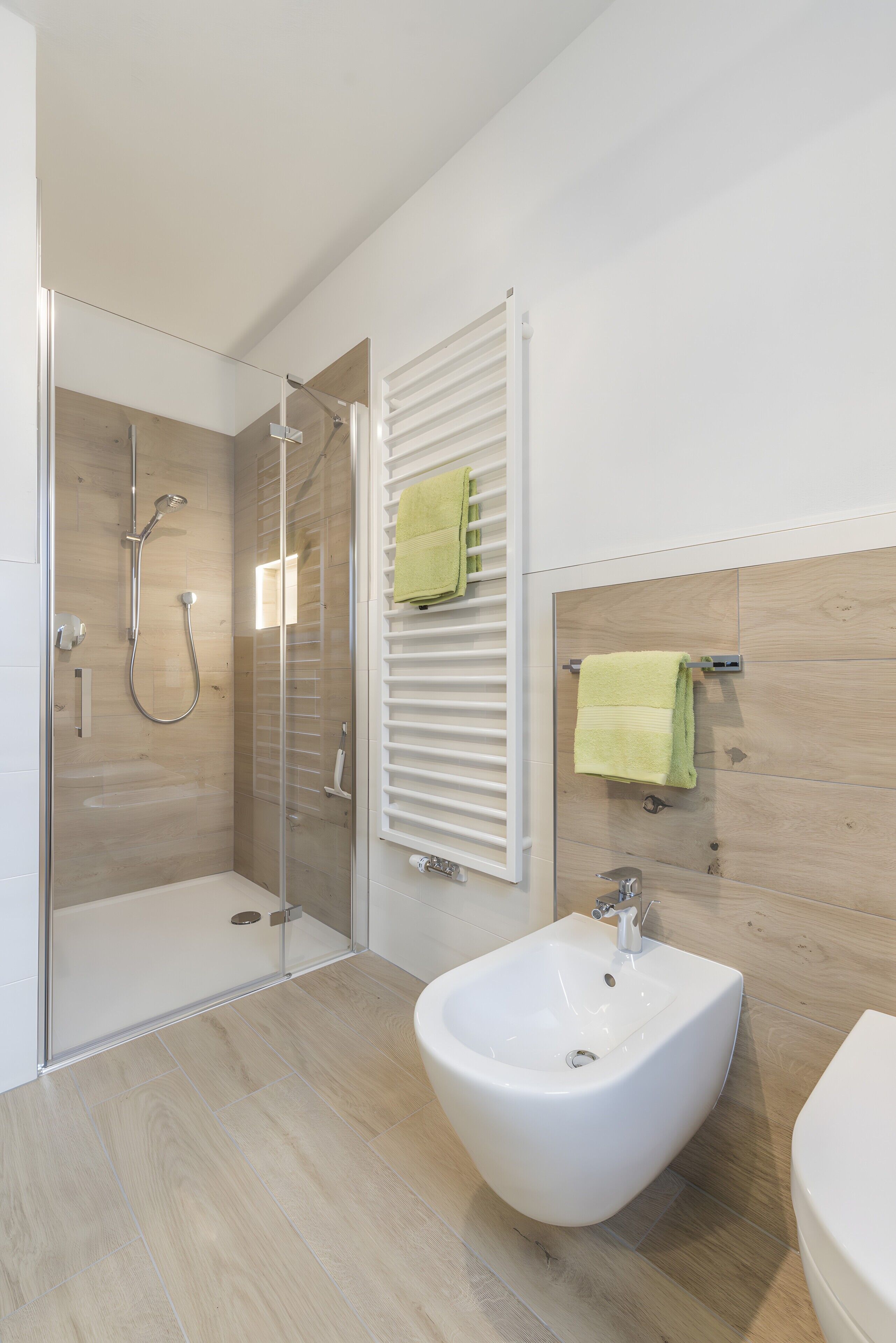 Un baño moderno con ducha envuelta en vidrio, un bidé y paneles de pared de madera.