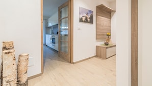 Un corridoio con una porta in legno che dà su una cucina, una panca di legno con una pianta e uno scaffale a parete.