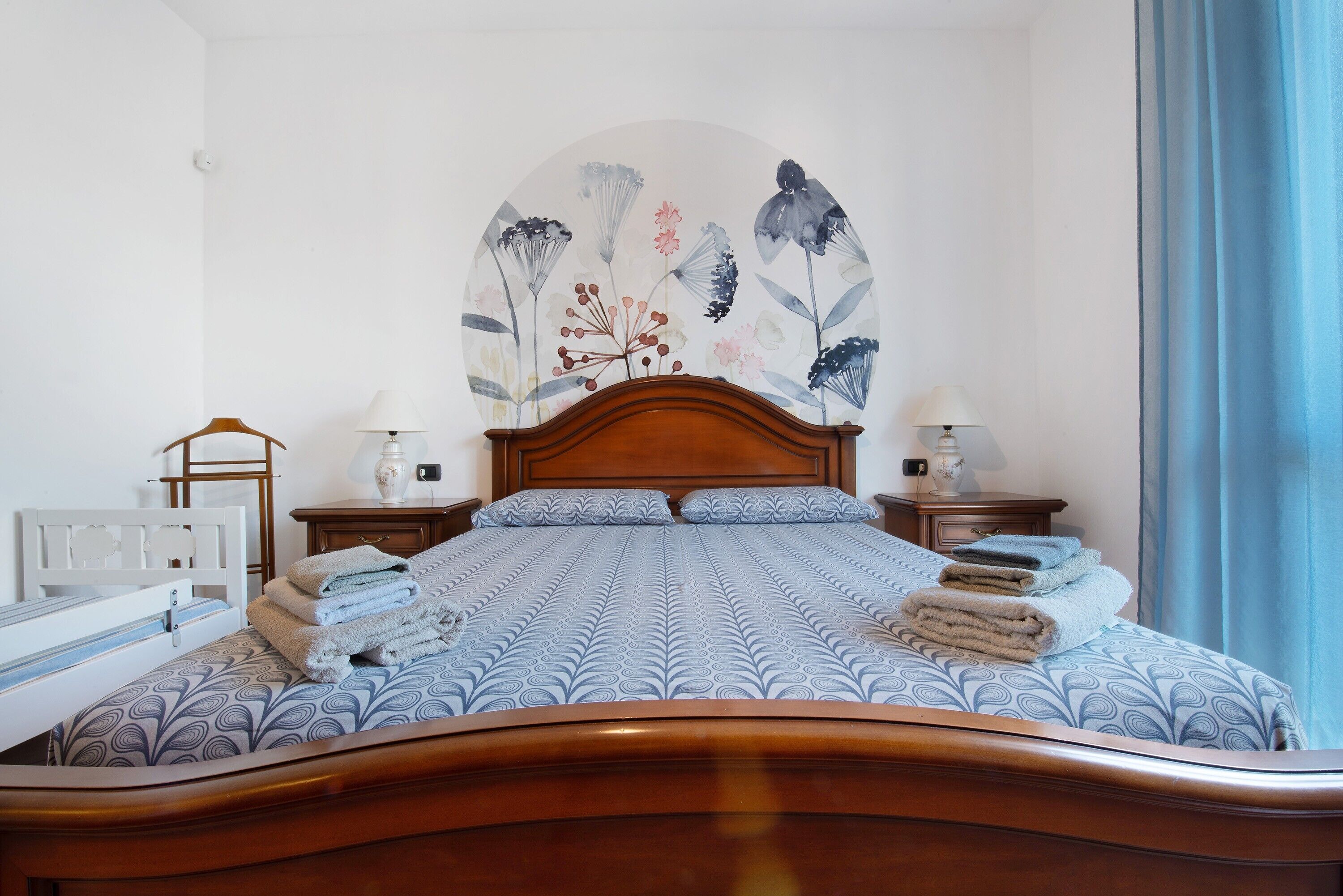 A neatly made bed with a patterned bedspread, a wooden headboard, and a wall-mounted artwork above it.