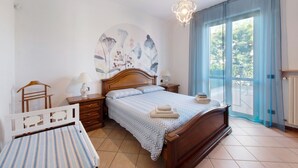 A bedroom with a bed, bedside tables, a nightstand, a chair, a window with curtains, and a wall mural.