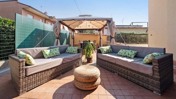 A patio area with wicker furniture, a woven ottoman, and a covered seating area.