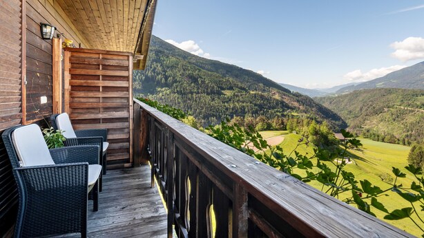A wooden deck with wicker chairs and a view of a mountainous landscape.
