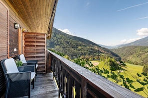 Una terraza de madera con sillas de mimbre y vistas a un paisaje montañoso.