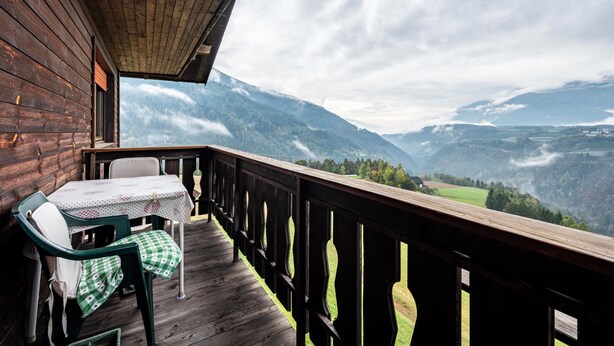 Una terraza de madera con una mesa y sillas, con vistas a un paisaje montañoso.