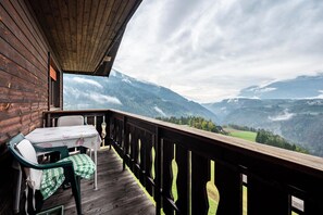 Une terrasse en bois avec une table et des chaises, offrant une vue sur un paysage montagneux.