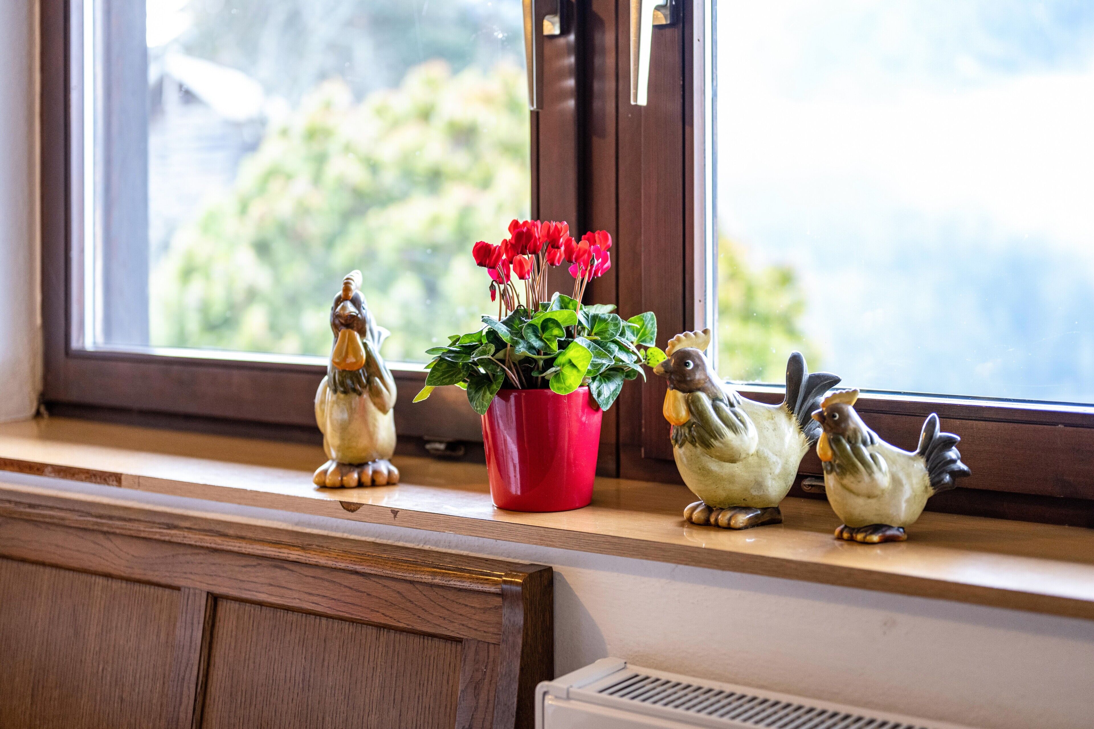 Ein Blumenkästen mit roten Blüten und zwei Vogelfiguren auf einem Fensterbrett.