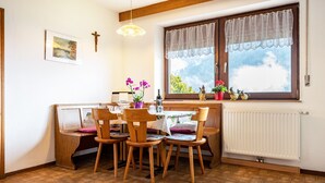 Un comedor con sillas de madera, una mesa, un ventanal con vistas, un radiador y una cruz en la pared.