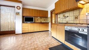 Una cocina con armarios de madera, salpicadero de azulejos, estufa y televisor.
