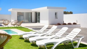 Ein moderner Außenpoolbereich mit Liegestühlen, einem kleinen Pool und einem Gebäude mit großen Fenstern.