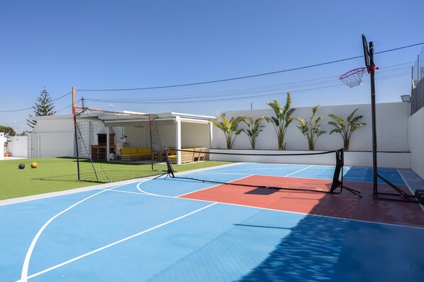 Un terrain de basket-ball en plein air avec un panier, un court de tennis et un espace de repos abrité.