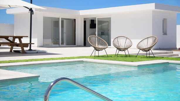Ein moderner Poolbereich mit klarem Pool, zwei Korbstühlen und einem Picknicktisch.