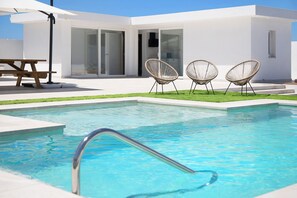 Un espace piscine moderne avec une piscine à eau claire, deux fauteuils en osier et une table de pique-nique.