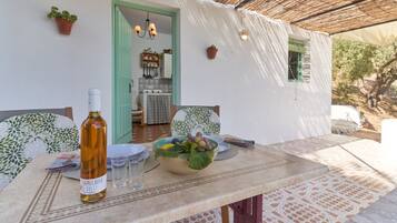 A dining table with a bottle of wine, a bowl of fruit, and a chair.