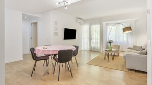A modern living room with a round dining table, a sofa, a TV, and a large window with curtains. - Apartment 'My Holidays Home' with Balcony, Wi-Fi and Air Conditioning (Palamós)