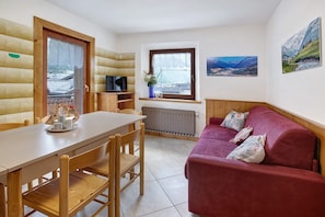 Une pièce comprenant une table à manger en bois, des chaises, un canapé rouge, une fenêtre donnant sur un beau paysage et un téléviseur fixé au mur.
