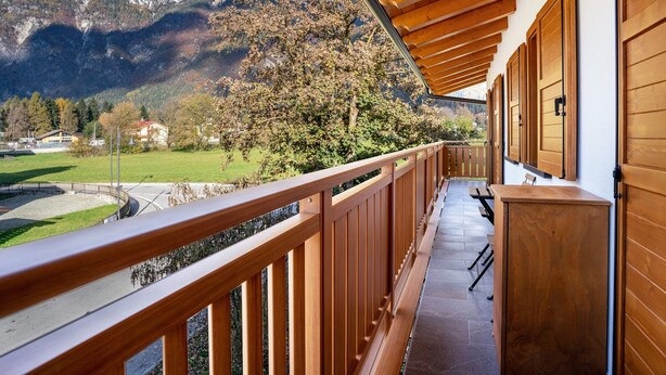 A balcony with wooden railings, a view of mountains, and a building with wooden doors.