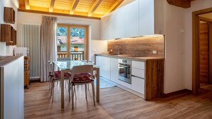 A modern kitchen with wooden beams, a dining area with chairs, and a view of a house through a window.