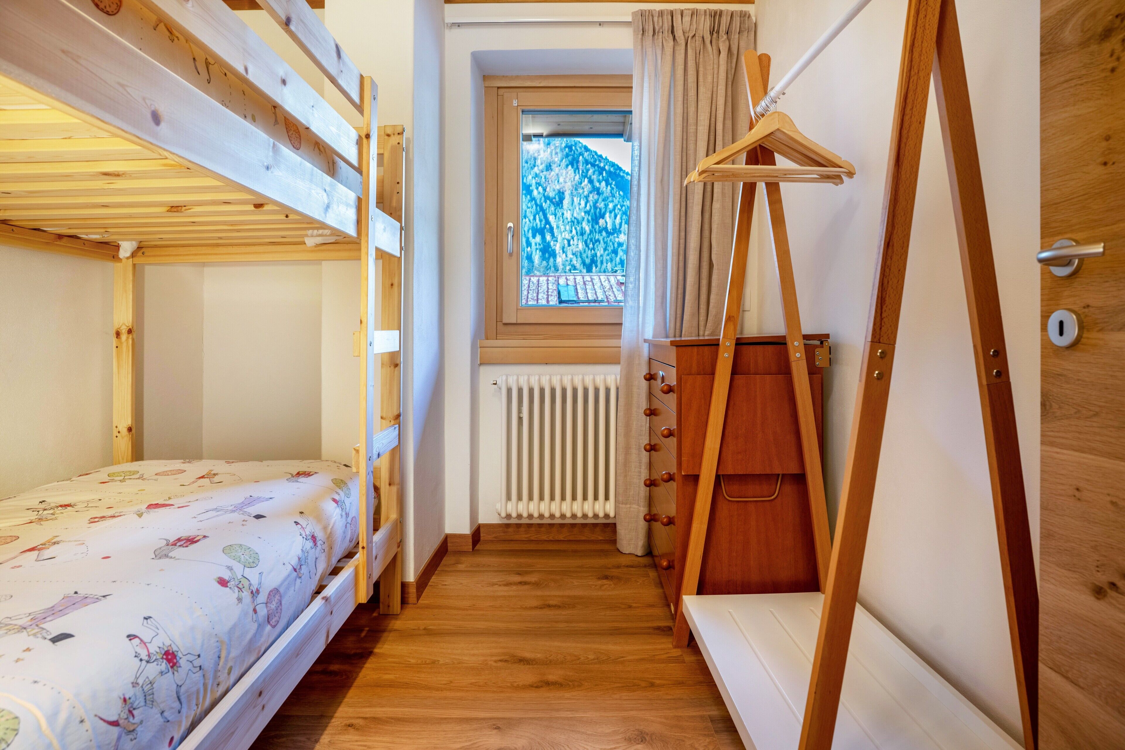 Ein Zimmer mit Etagenbetten, einem Holzschrank, einem Heizkörper und einem Fenster mit Bergblick.