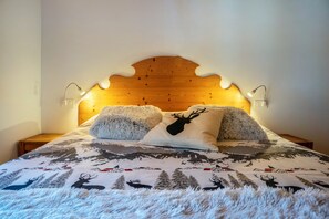 A bed with a wooden headboard, two wall-mounted reading lamps, and a patterned bedspread.