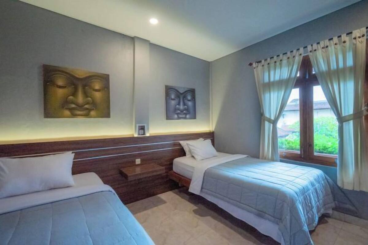 A hotel room with two beds, a window with curtains, and wall art.