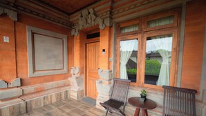 A room with a wooden floor, a large window with curtains, a wooden door, and a small table with a potted plant. - Nobody Inn Bali (Ubud)