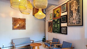 A room with a sofa, chairs, a round wooden table, and wall-mounted artwork. - Nobody Inn Bali (Ubud)