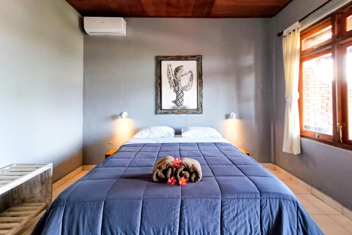 A bedroom with a blue bedspread, a framed artwork on the wall, and a window with curtains.