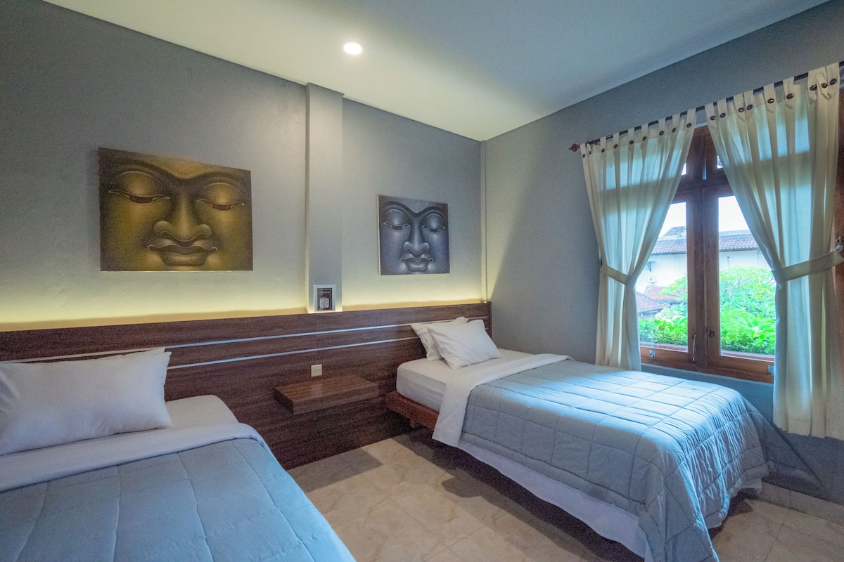 A hotel room with two beds, a window with curtains, and artwork on the wall.