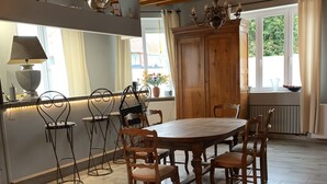 A dining area with a wooden table and chairs, a chandelier, and a view of the outdoors through a window. - Villa Marguerite, à 12 Minutes de la Plage ! (Cormont)