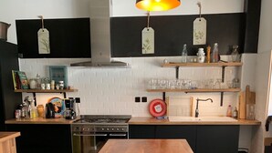 A modern kitchen with a wooden table, black cabinets, and a hanging pendant light. - Villa Marguerite, à 12 Minutes de la Plage ! (Cormont)