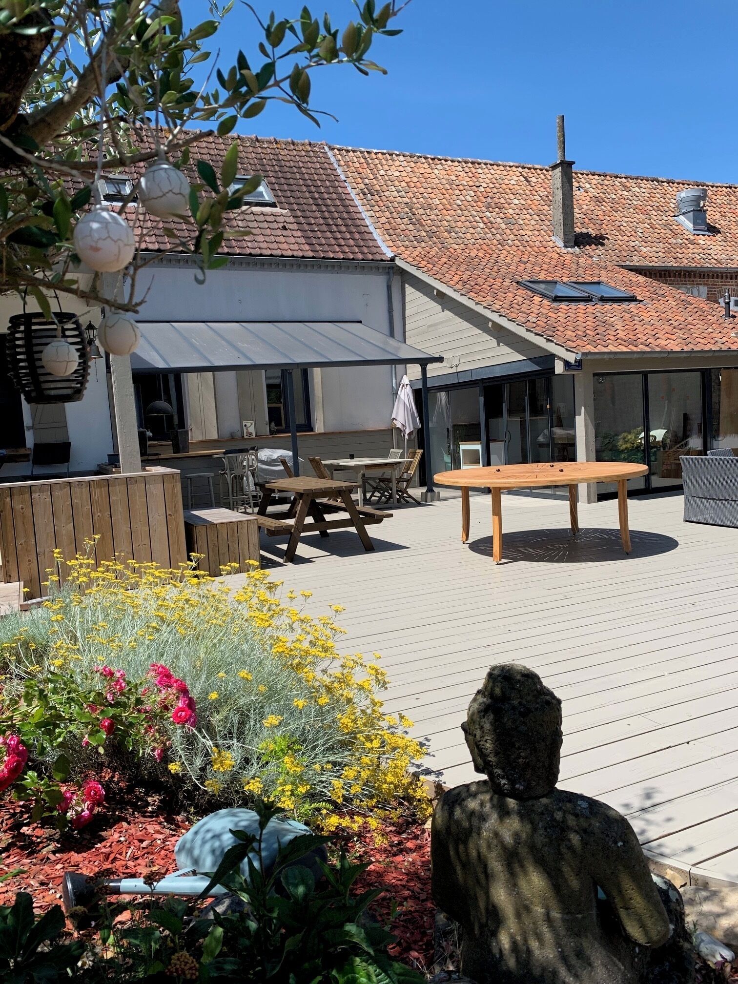 A patio area with outdoor furniture, a stone statue, and a garden with flowers.