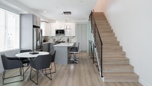 Een moderne keuken met een centraal eiland, een eethoek met stoelen en een trap.