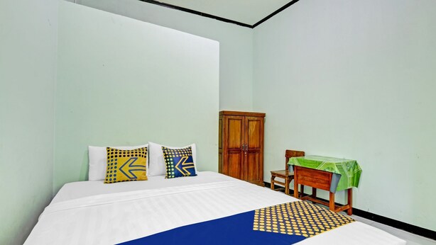 Une chambre à coucher avec un lit, deux oreillers, une armoire en bois et une petite table recouverte d’une nappe verte.