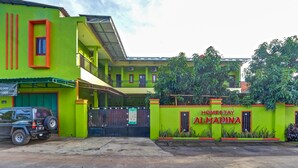 Un bâtiment vert avec une enseigne indiquant « Homestay Almadina » et un VUS garé devant.