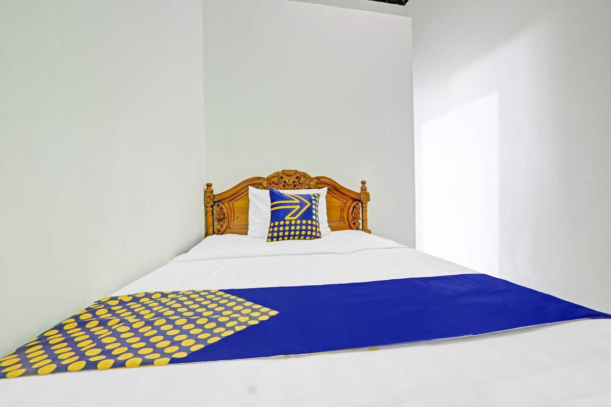 A bed with a wooden headboard, white bedding, and a blue and yellow patterned throw.