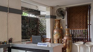 A reception area with a desk labeled "RECEPTIONIST," a laptop, a large decorative vase, and two bar stools.