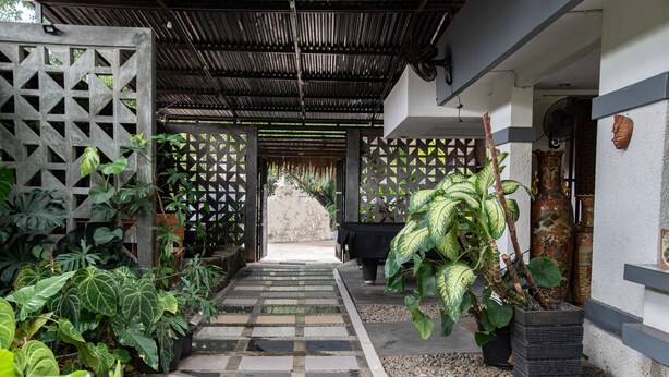 A covered outdoor pathway leading to a building entrance, surrounded by potted plants and a decorative fence.