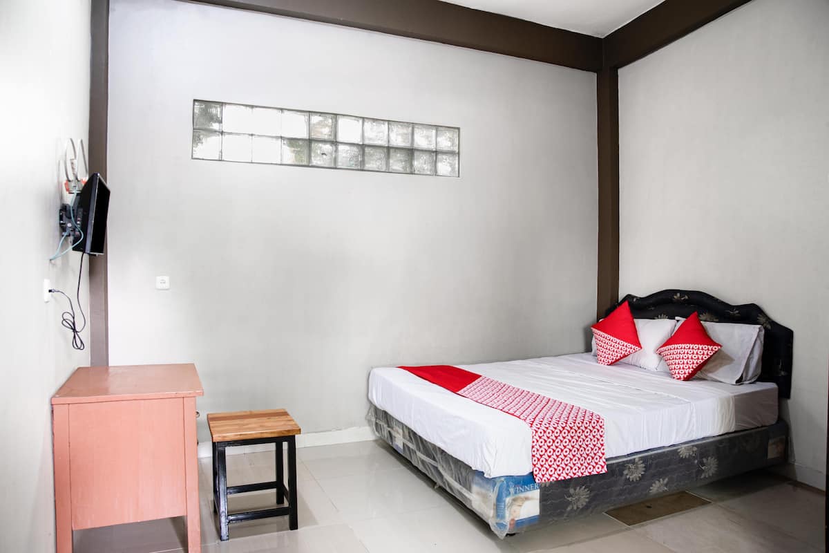 A bedroom with a bed, a small desk, and a wall-mounted shelf.