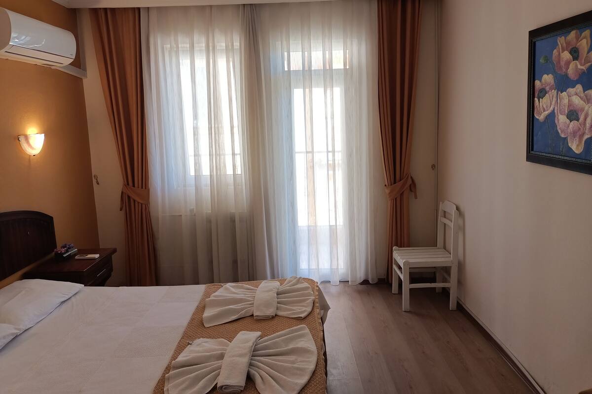 Une chambre d’hôtel avec un lit, une chaise, un tableau et une fenêtre avec des rideaux.