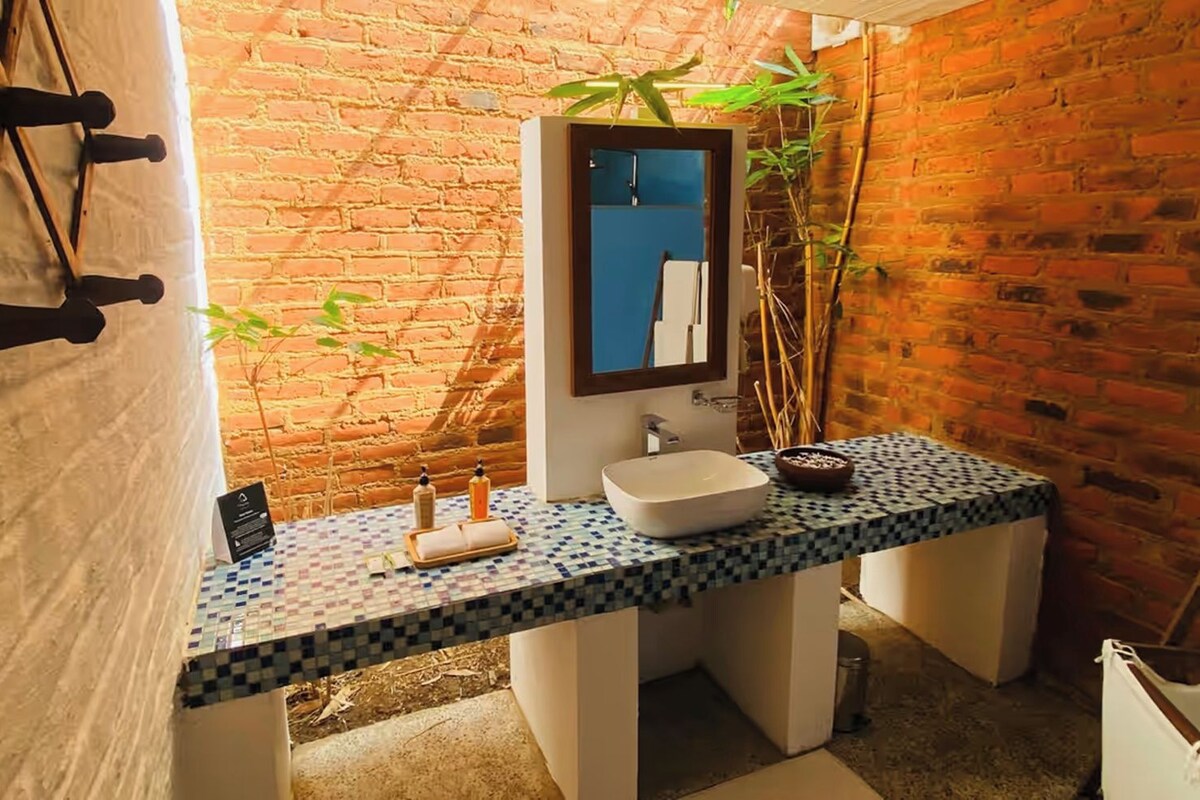 Une salle de bain avec un comptoir carrelé, un lavabo blanc, un miroir et une plante en pot.