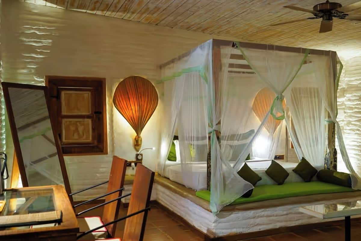 Quarto com cama de dossel, ventoinha no teto e chão de madeira rústica.