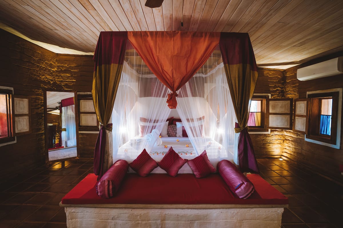 Quarto com cama sob um dossel, paredes de pedra e teto de madeira.