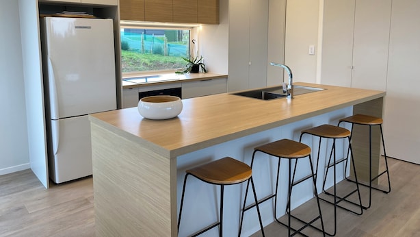 Uma cozinha moderna com uma ilha central, banquetas, uma pia embutida e uma geladeira.