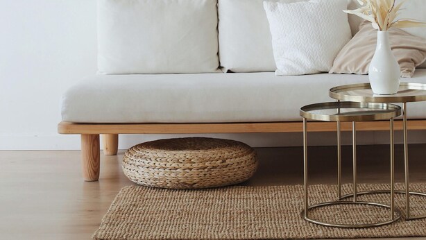 Ein schlicht eingerichtetes Wohnzimmer mit einem weißen Sofa, einem runden Metall-Couchtisch und einem gewebten Korb auf einem Teppich.
