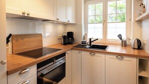 Una cocina moderna con armarios blancos, encimera de madera, horno empotrado, cocina, cafetera y ventana con vistas a zonas verdes.